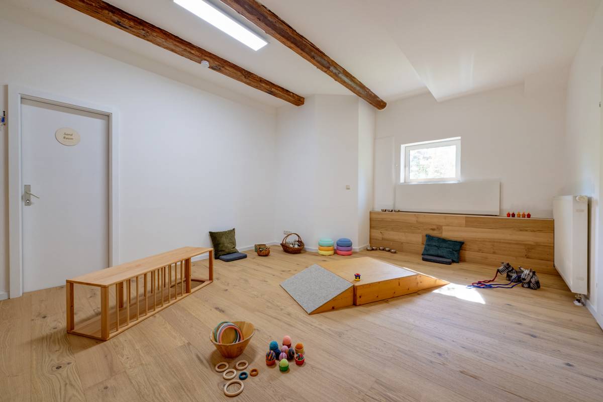 Heller, leerer Raum im IM MITEINANDER mit Holzboden, sichtbaren Deckenbalken und einer Sitzbank aus Holz an der Wand