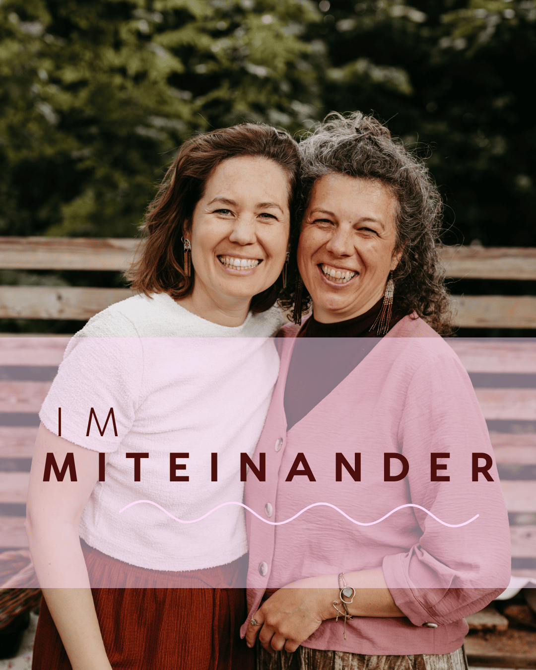 Felicitas Matzer und Anja Tlapak, die beiden Ansprechpersonen des IM MITEINANDER, stehen lächelnd Wange an Wange vor einer Holzwand
